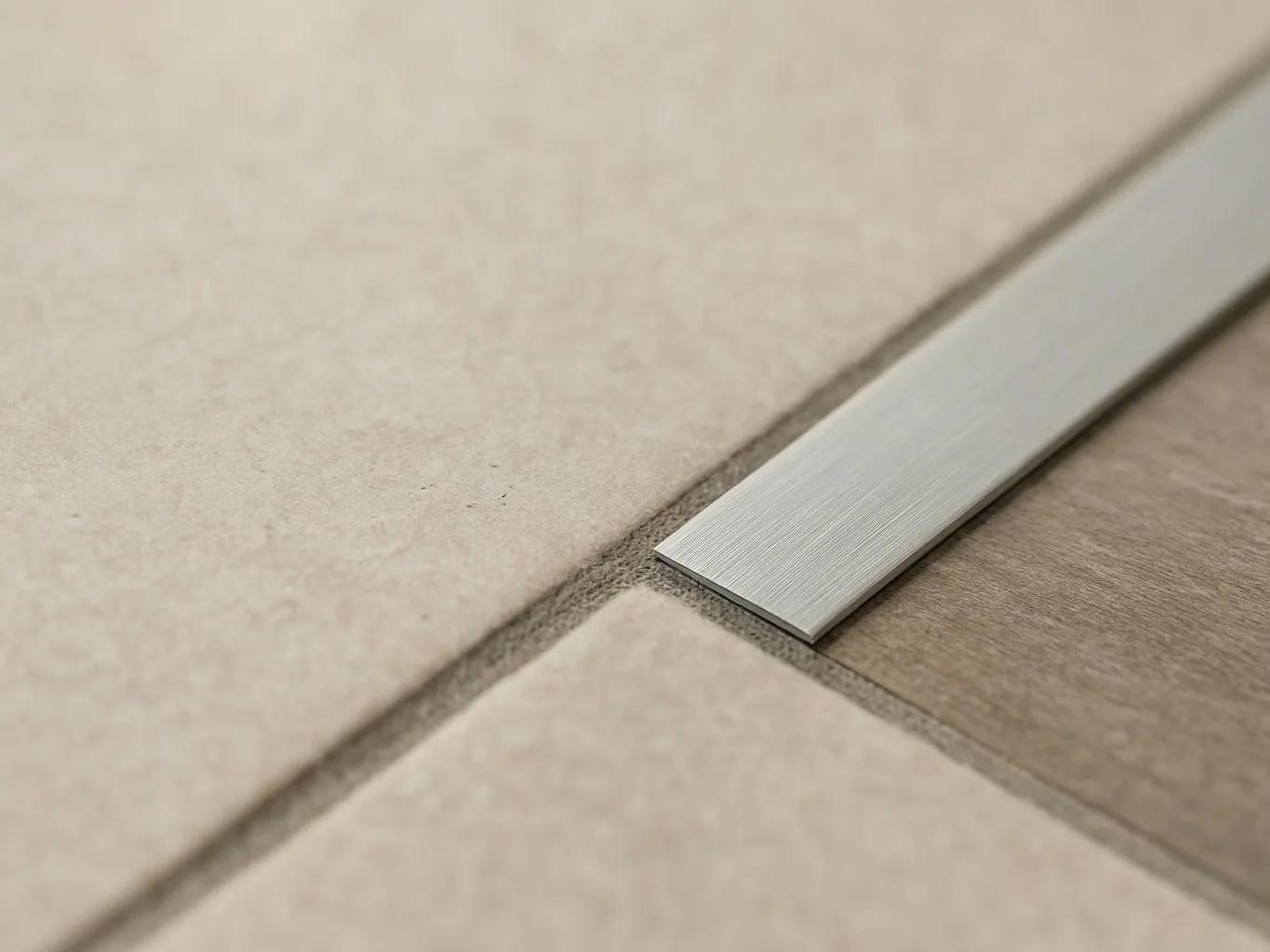 A brushed metal strip joins two beige floor tiles in a close-up view