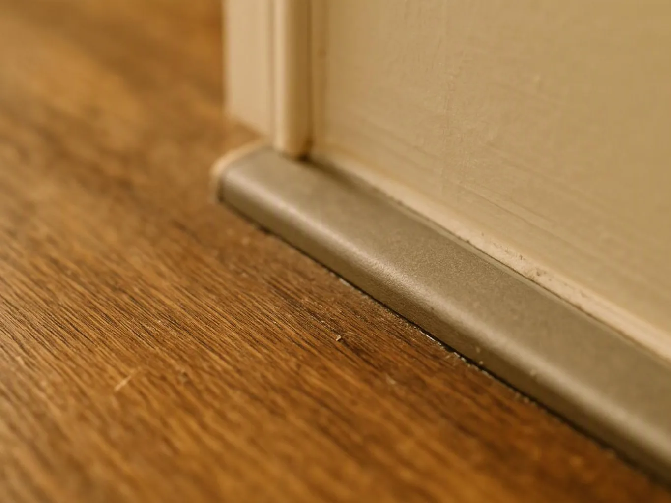 A close-up shows a door bottom seal beside a hardwood floor indoors