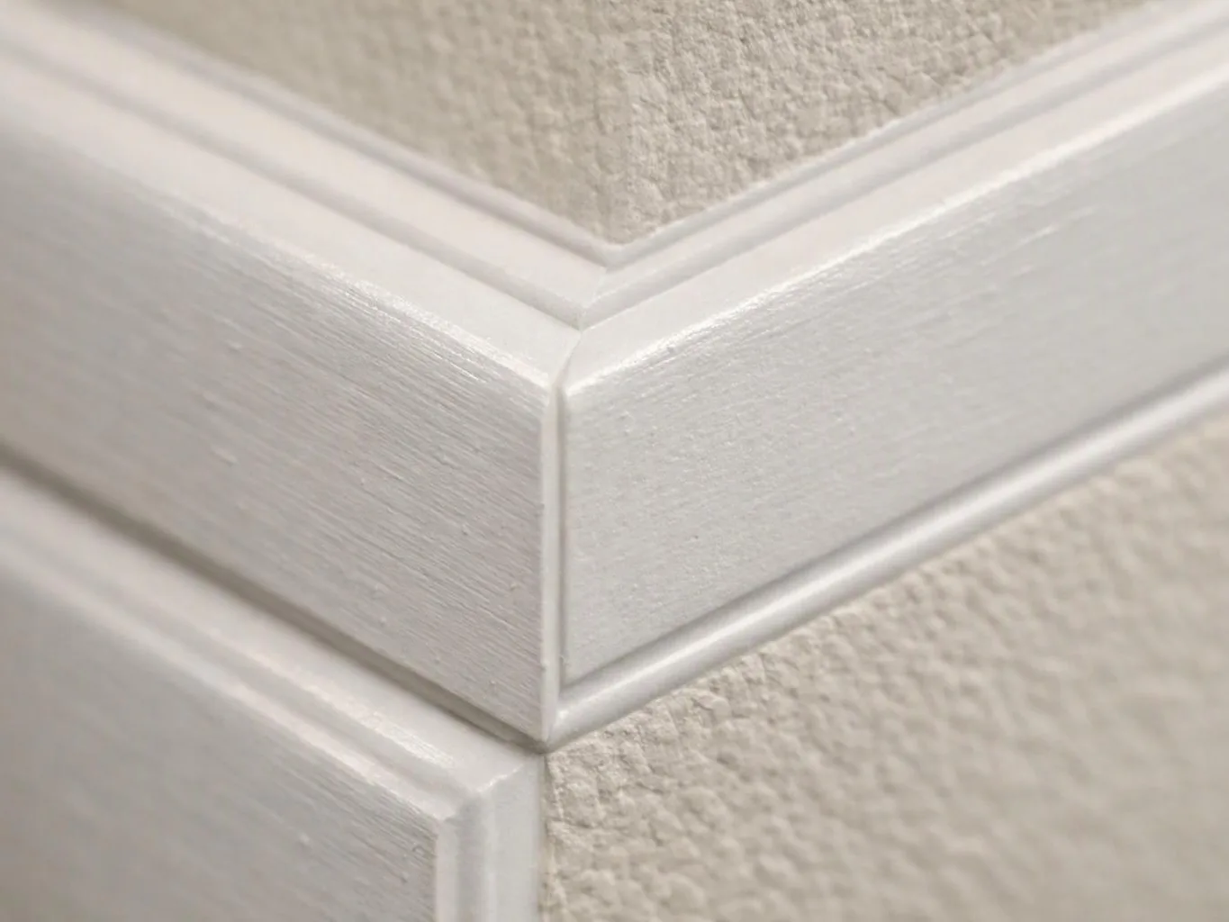 Close-up of white painted trim meeting at a sharp corner against a textured beige wall