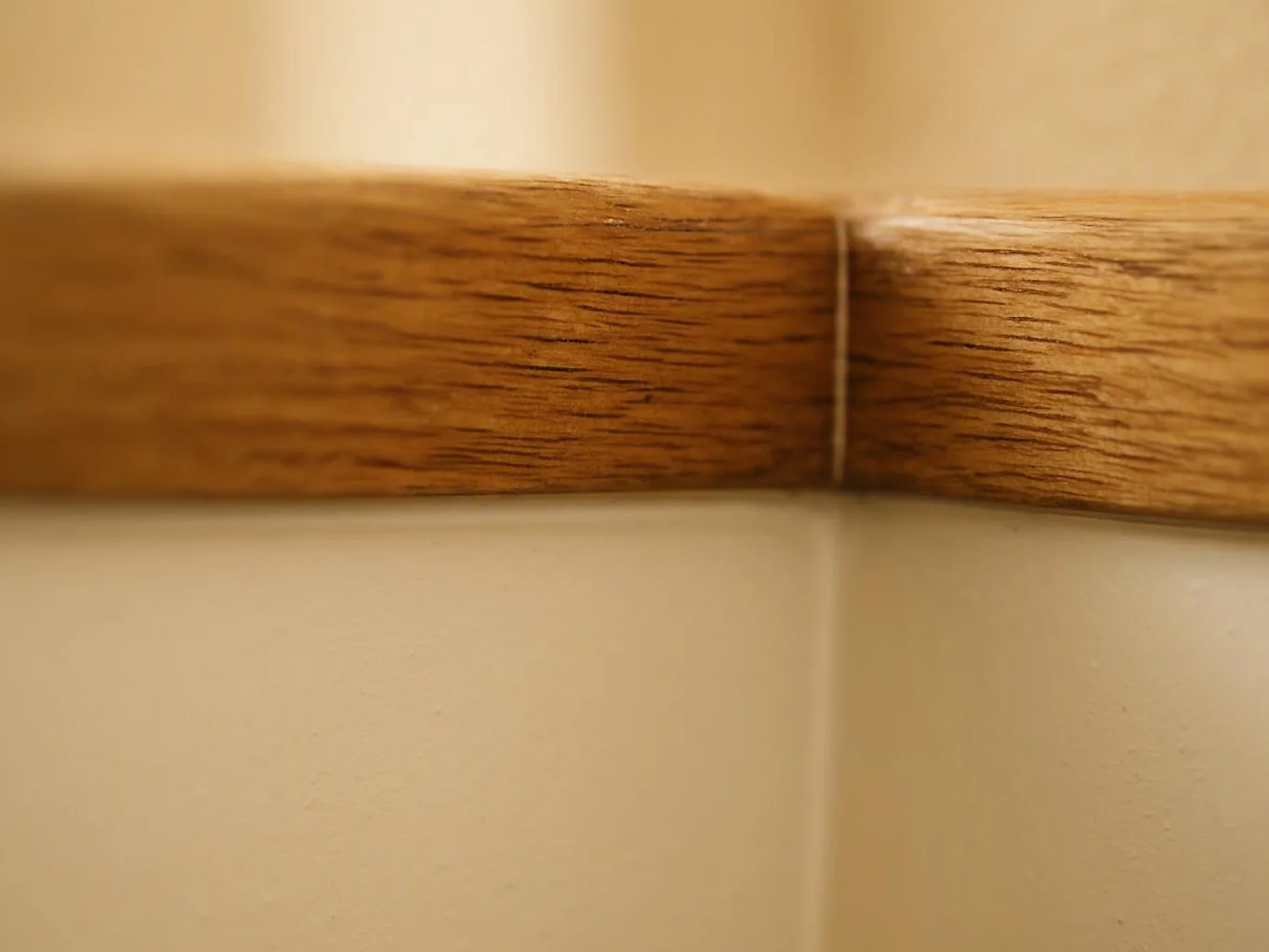 Close-up of a wooden trim piece meeting a cream-colored wall corner indoors